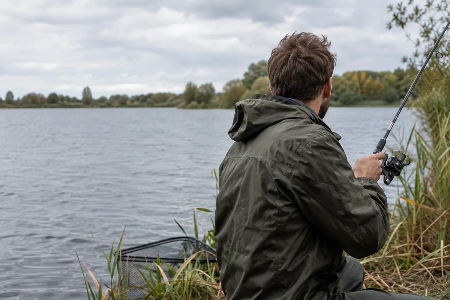 Angler mit Spinnrute und Kescher am natürlichen Seeufer